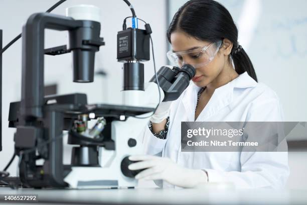 human genetics and genomic medicine research and development. asian laboratory technician looking through microscope while examining genomic sample during research in laboratory. - genomics stock-fotos und bilder