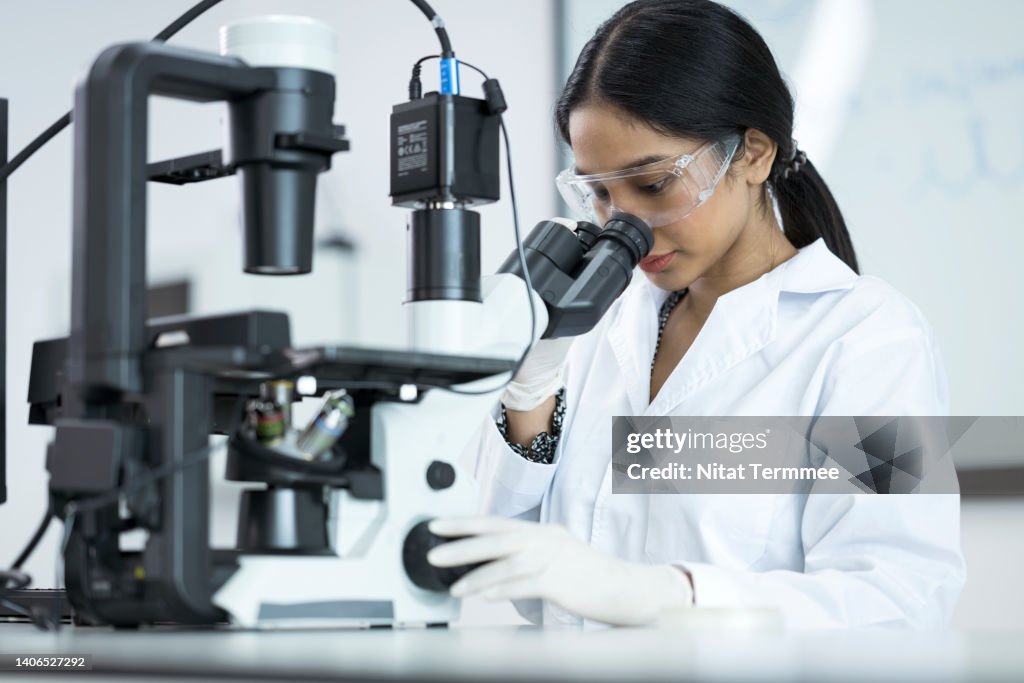 Human Genetics and Genomic Medicine Research and Development. Asian Laboratory technician looking through microscope while examining genomic sample during research in laboratory.