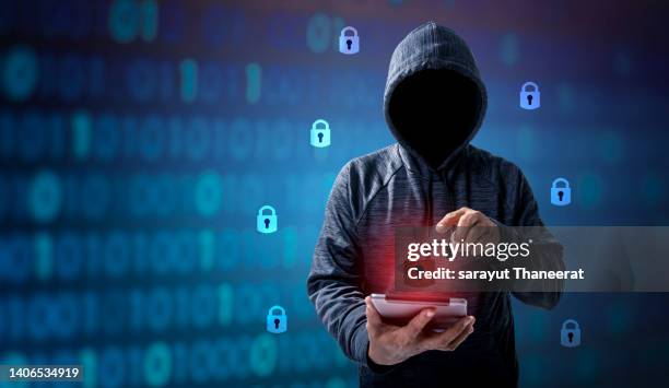 hacker in hoodie dark theme hacker in a blue hoody standing in front of a coding background with binary streams and information security terms cybersecurity concept - anonymous hacker stockfoto's en -beelden