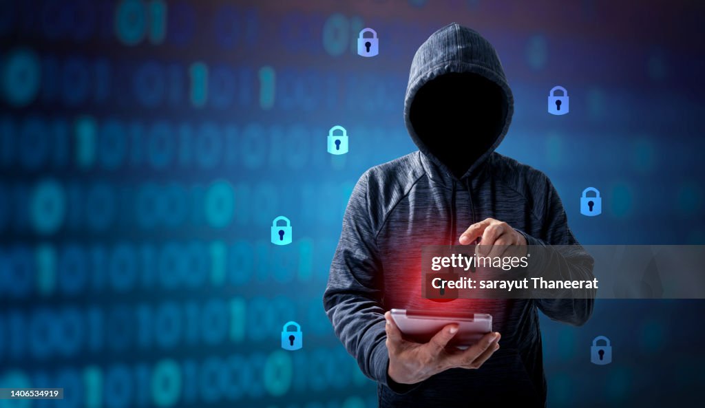 Hacker in hoodie dark theme Hacker in a blue hoody standing in front of a coding background with binary streams and information security terms cybersecurity concept