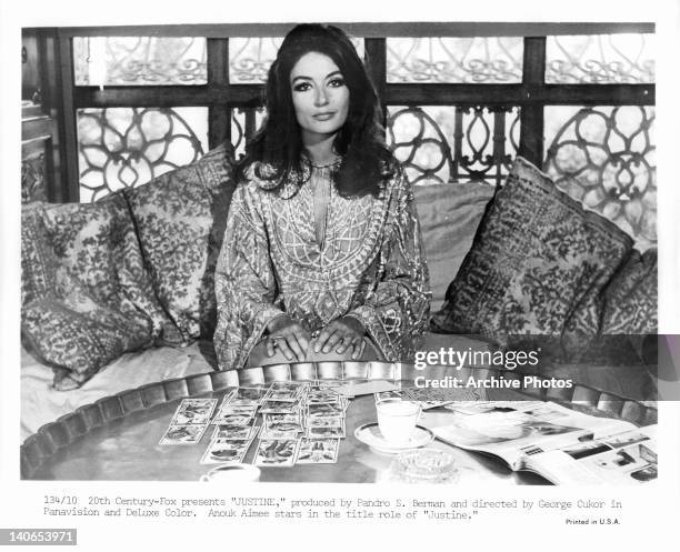 Anouk Aimee sitting before table full of cards in a scene from the film 'Justine', 1969.