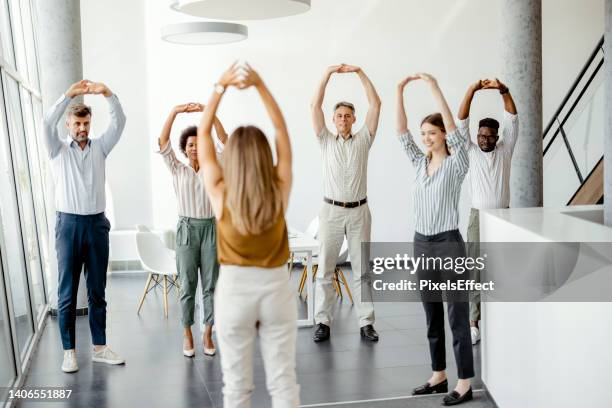 uomini d'affari che fanno esercizio di stretching sul posto di lavoro - sport office foto e immagini stock