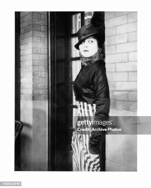 Theda Bara leaning against brick wall in a scene from the film 'A Fool There Was', 1915.