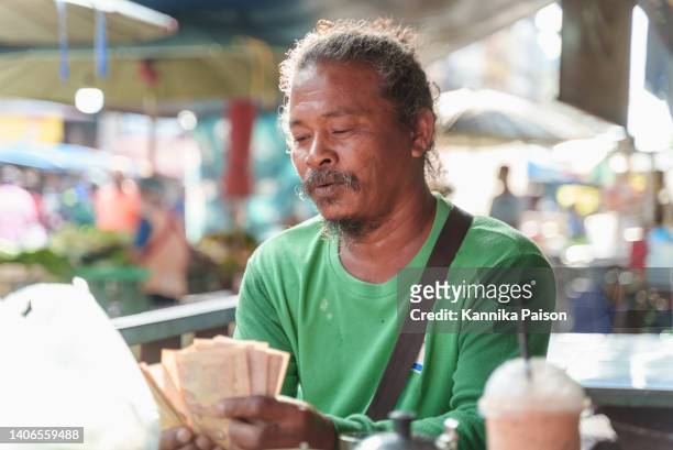 senior asian man worker feeling happy holding wad of money after raise a loan from local commercial bank. - money borrow stock pictures, royalty-free photos & images