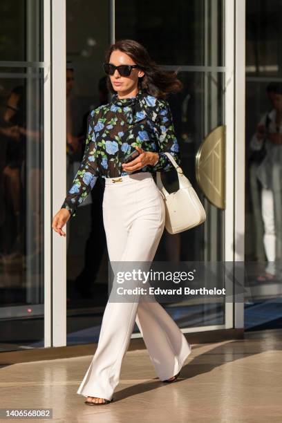 Guest wears black sunglasses, a black tulle with green and blue flower print pattern high neck / long sleeves blouse, a white latte varnished leather...