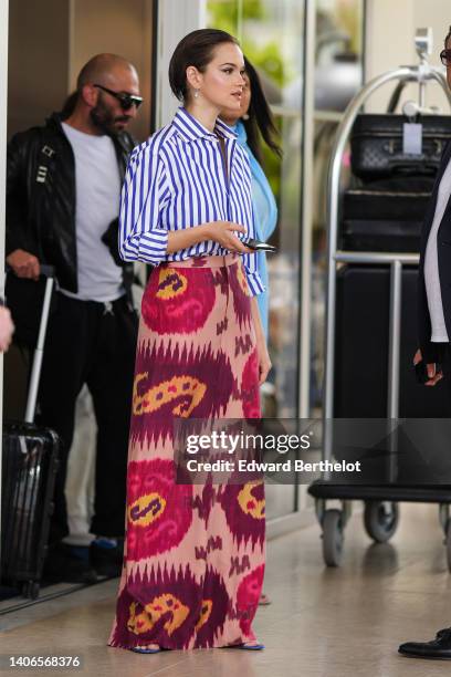 Guest wears silver and flower pendant earrings, a navy blue and white striped print pattern shirt, a pale red / burgundy / red / yellow print pattern...