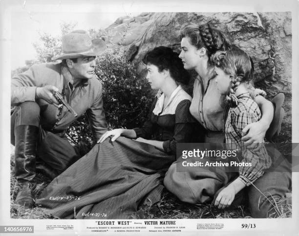 Victor Mature talking to a hiding Faith Domergue, Elaine Stewart, and child in a scene from the film 'Escort West', 1958.