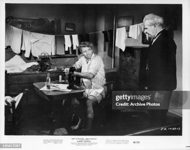 Burt Lancaster talking to unidentified man as he dries wet clothes on line hanging across his room in a scene from the film 'Elmer Gantry', 1960.