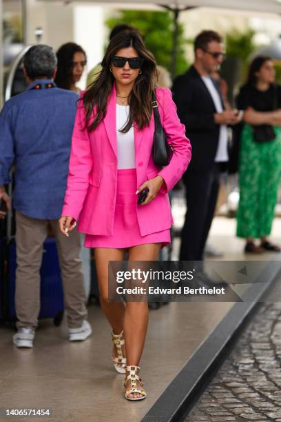 Guest wears black sunglasses, gold earrings, gold chain pendant necklaces, a white tank-top, a neon pink long blazer jacket, neon pink short skirt, a...