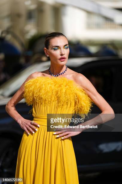 Guest wears diamond earrings, a navy blue sapphire and diamond necklace, a yellow feather shoulder-off / long pleated / belted dress, during the 75th...