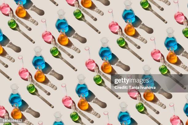 pattern of laboratory glassware with multicolored liquids on beige background. natural medicine, cosmetic research, bioscience, organic skin care products. top view, flat lay. - boiling flask stock pictures, royalty-free photos & images