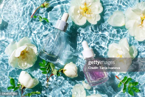 glass bottles of nature cosmetic serum with a pipette, facial essence with white rose flowers on a background of blue water with waves. beauty products for body and face care. - white rose flower stock pictures, royalty-free photos & images