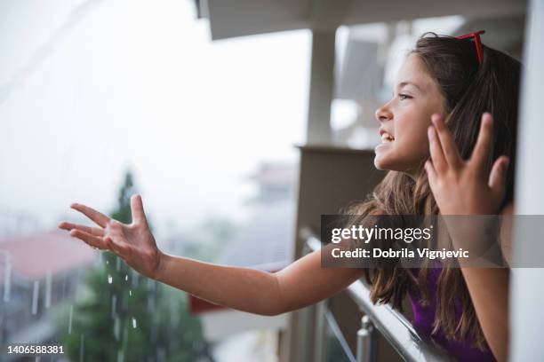 child standing on a balcony, looking at the rain pouring and shouting in anger - standing in the rain girl stock pictures, royalty-free photos & images