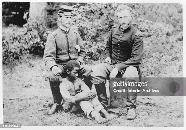 Captain George Armstrong Custer of the 5th Cavalry sits with a Confederate prisoner, Lieutenant James B Washington and his slave, in Fair Oaks, VA,...