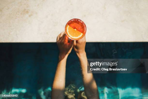 woman hands holding spritz cocktail on poolside close-up. leisure and relaxation concept, cold summer drink - spritz drink stock pictures, royalty-free photos & images