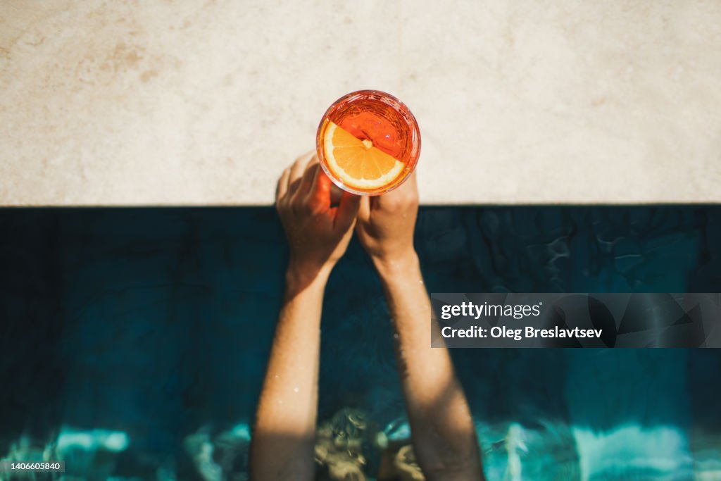 Woman hands holding Spritz cocktail on poolside close-up. Leisure and relaxation concept, cold summer drink