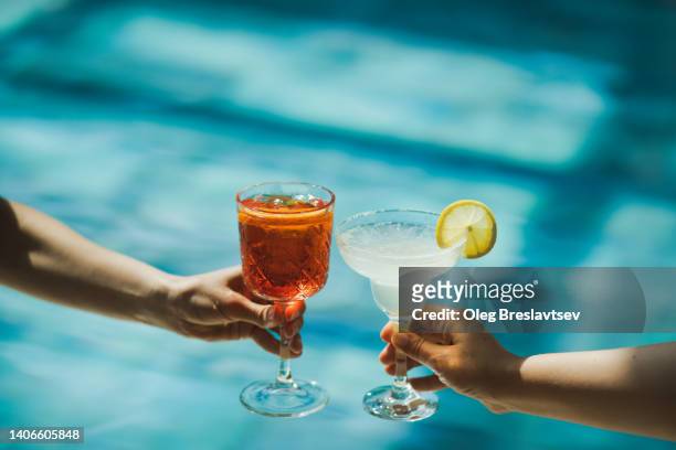 two hands toasting with glasses spritz and margarita cocktails on background of swimming pool. cheers - drinken stockfoto's en -beelden