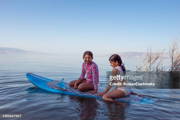 elementary-age two girls having fun on a stand-up paddleboard (sup). - kids swimwear stock pictures, royalty-free photos & images