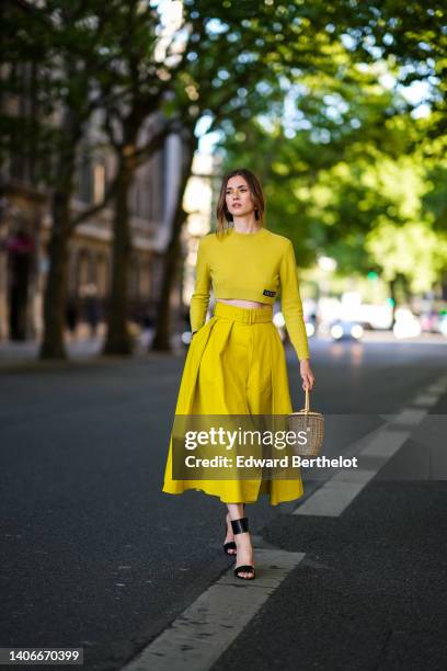 Zita d'Hauteville wears gold earrings, a gold chain necklace, a yellow wool cropped pullover from Patou, a matching yellow high waist / pleated midi...