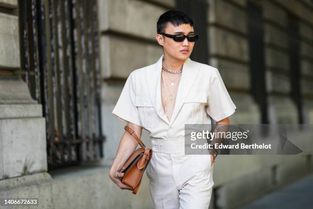 Jeck Aguilar wears black sunglasses, a silver large chain necklace, gold chain pendant necklaces, a white V-neck / short sleeves shirt, high waist...