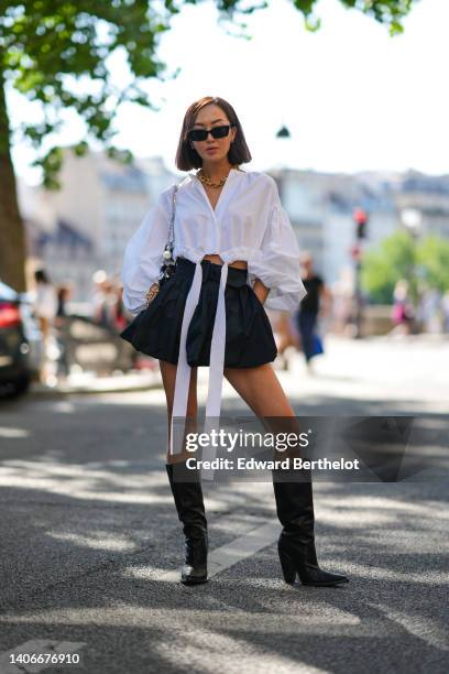 Chriselle Lim wears black sunglasses, silver earrings, a gold large chain necklace, a white puffy sleeves / cropped fringed shirt, a silver 1969 Nano...