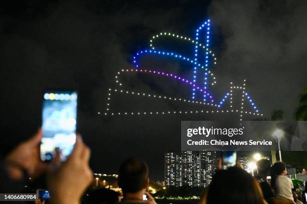 People take photos as drones form a pattern featuring 'Lookout tower' over Tai Po Waterfront Park to celebrate the 25th anniversary of Hong Kong's...