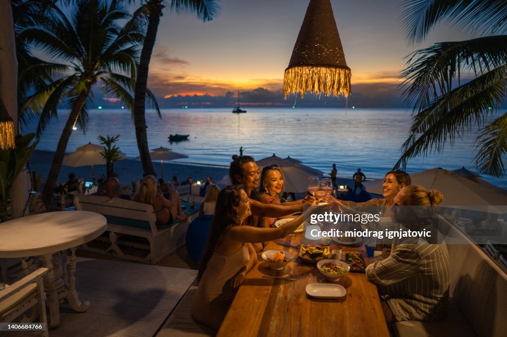 Multiracial friends at the dinner at the beach restaurant toasting with wine
