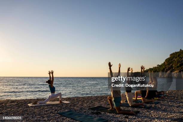 group of people practicing yoga on the beach at sunrise - sunrise yoga stock pictures, royalty-free photos & images