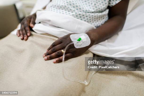 close up iv drip in hand man in hospital bed - iv infuus stockfoto's en -beelden