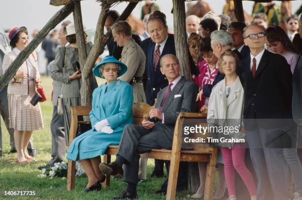 Queen Elizabeth II sits beside Prince Philip on a bench in front of a crowd of people during a royal tour in Bugac, Hungary, 6th May 1993.