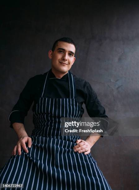 smiling caucasian chef wearing an apron and looking at camera (studio shot with dark background) - chef patissier stock pictures, royalty-free photos & images