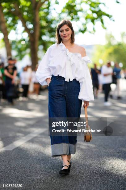 Guest wears a white ruffled shoulder-off / puffy long sleeves shirt, navy blue denim rolled-up large pants, a brown shiny leather handbag, black...