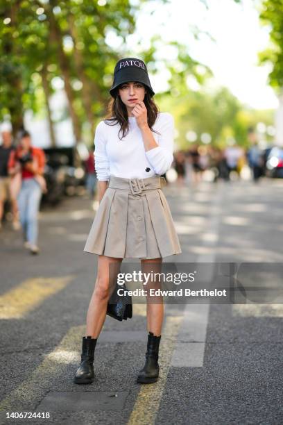 Guest wears a black with embroidered white inscription bob hat from Patou, a white ribbed long sleeves t-shirt, a beige pleated / belted / buttoned...