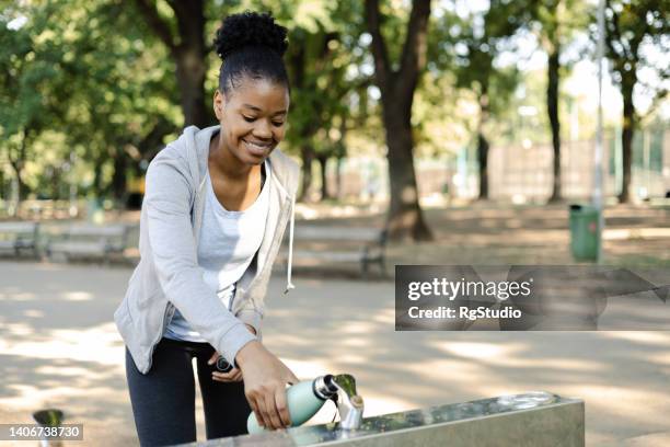 beautiful african girl pouring water at the drinking fountain after jogging - african ethnicity photos stock pictures, royalty-free photos & images