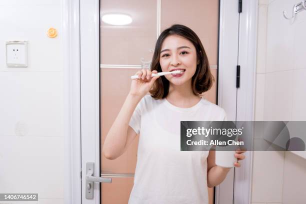 asian young woman brushing her teeth in front of mirror - 歯みがき粉 ストックフォトと画像