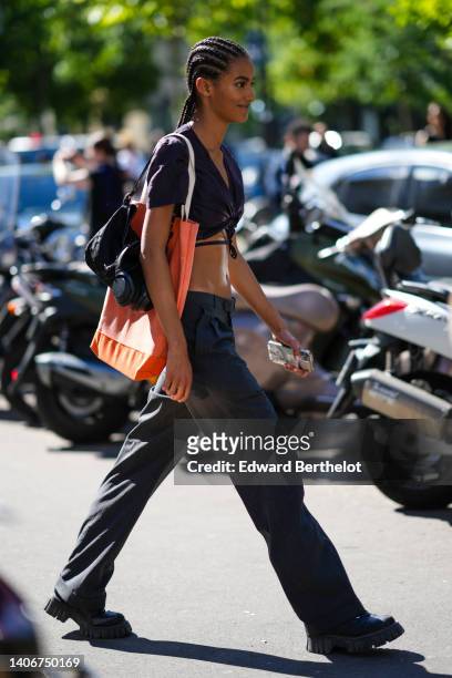 Model wears a black V-neck / lace waist / short sleeves t-shirt, a black shoulder bag, an orange oversized shoulder bag, black suit pants, black...
