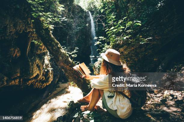 woman writing and reading travel notes against waterfall. - trip diary stock pictures, royalty-free photos & images