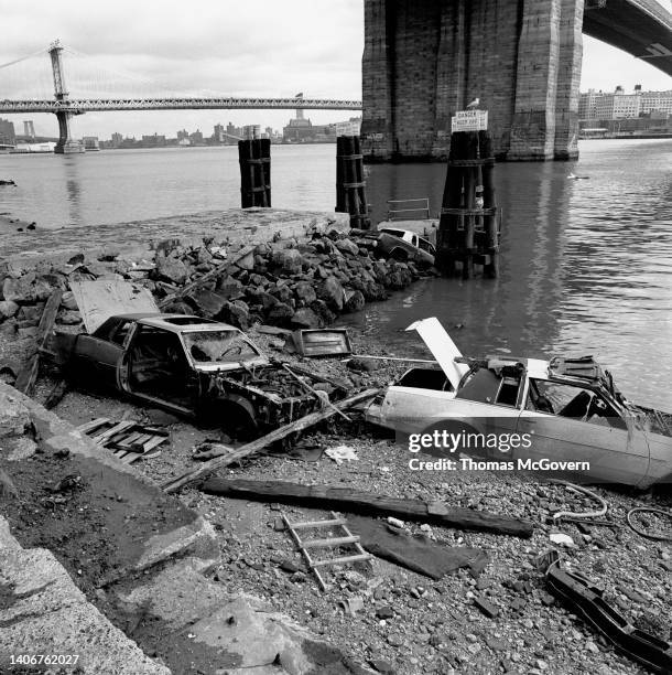 Two abandoned cars under the Brooklyn Bridge with Manhattan Bridge and East River in background in 1990 in Manhattan in New York.