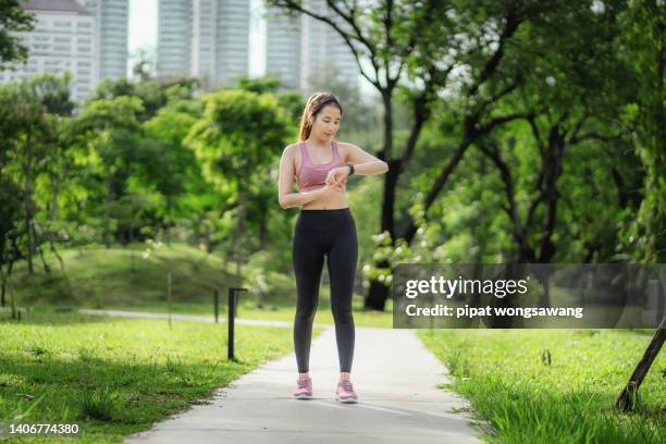 beautiful asian runner looks at her smart watch in a park. after jogging to check if health is still in good shape or not. concept of urban society and health care - still life stockfoto's en -beelden