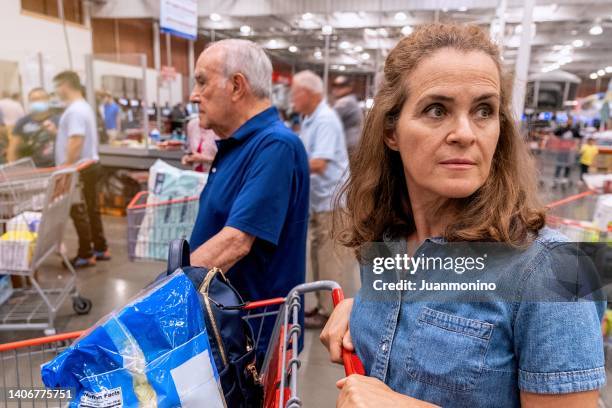 mujer madura sosteniendo su carrito de compras esperando en la fila para pagar en una megatienda - superalmacén fotografías e imágenes de stock