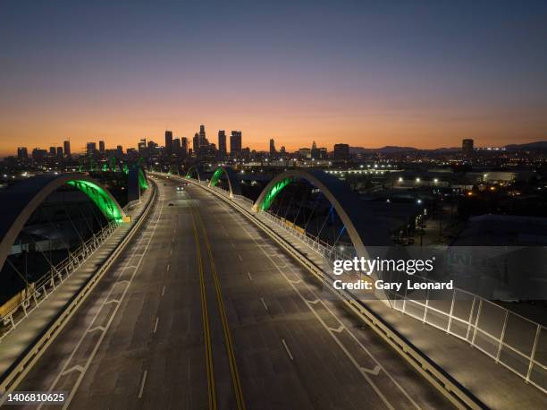 The night downtown skyline glows deep orange and on the bridge an LED lighting test illuminates the arches emerald green during the construction of...