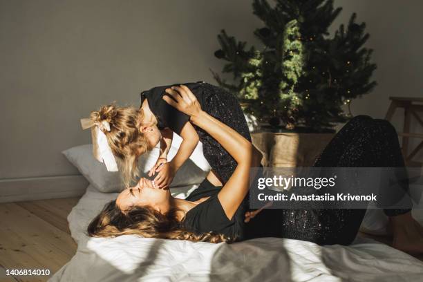 beautiful mother and daughter having fun at home in bed near the christmas tree. - mother and daughter making the bed stock pictures, royalty-free photos & images