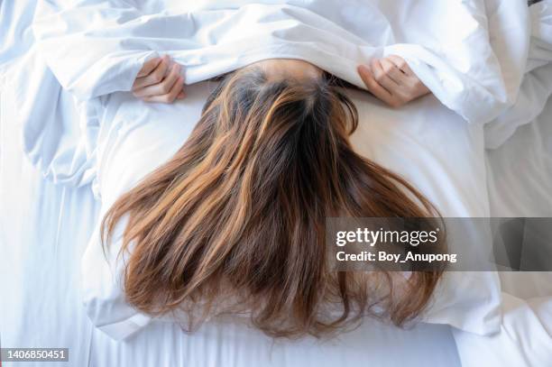 woman with long hair hiding under blanket while sleeping on bed. - woman pillow over head stock pictures, royalty-free photos & images