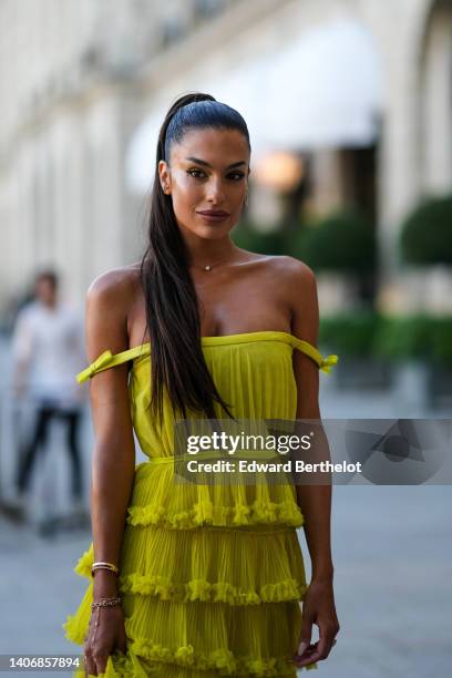 Jessica Aïdi Verratti wears a gold and diamonds earring, a gold chain pendant necklace, a yellow shoulder-off / ruffled pleated long dress, a gold...