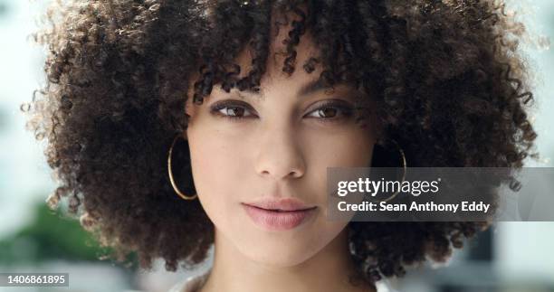 portrait of a beautiful woman's face with afro curly hair and brown eyes. one stylish and confident mixed race female with cool hairstyle, trendy makeup and hoop earrings standing outside in the city - earring stock pictures, royalty-free photos & images
