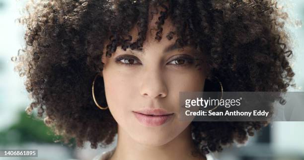 portrait of a beautiful woman's face with afro curly hair and brown eyes. one stylish and confident mixed race female with cool hairstyle, trendy makeup and hoop earrings standing outside in the city - earring 個照片及圖片檔