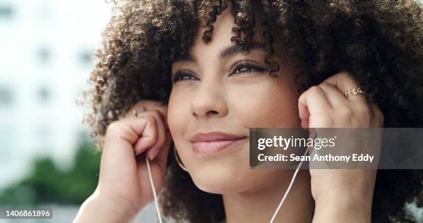 nahaufnahme einer glücklichen jungen frau mit lockigem haar, die lieblingsmusiklieder oder podcasts mit kopfhörern in der stadt im freien hört. gesicht der frau, die spaß beim erkunden und reisen in der stadt hat - hineinstecken stock-fotos und bilder