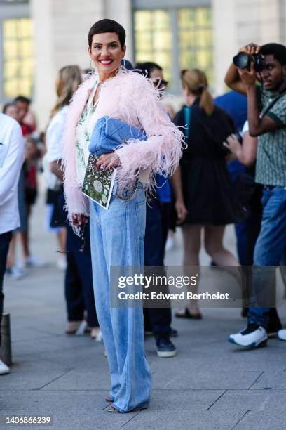 Cristina Cordula wears silver earrings, a white with green flower print pattern silk shirt, a pale pink feather jacket, a blue denim Chanel 19...