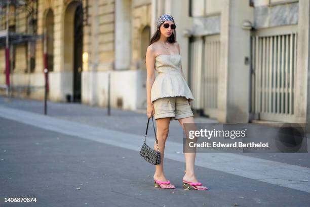 Gabriella Berdugo wears a blue and beige Dior Oblique Jacquard print pattern silk scarf from Dior, black sunglasses, gold chain pendant earrings, a...