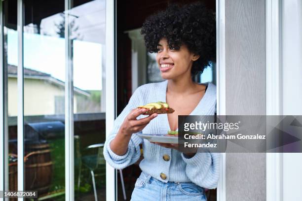 young hispanic woman enjoys a healthy lunch outside a home - eating bread stockfoto's en -beelden